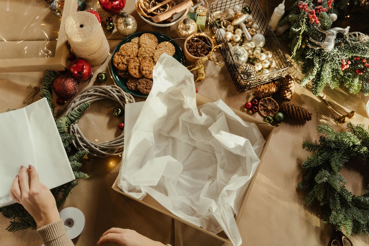 Hands preparing holiday gifts with cookies and decorations in a Christmas workshop setting.